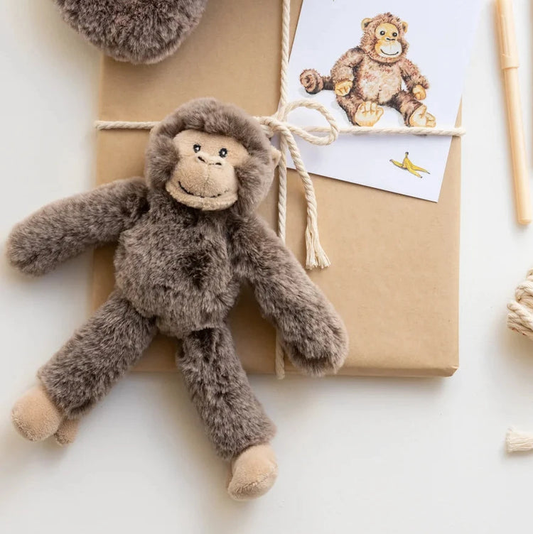 plush monkey toy rattle on brown paper with a card featuring another monkey illustration, on a light background.