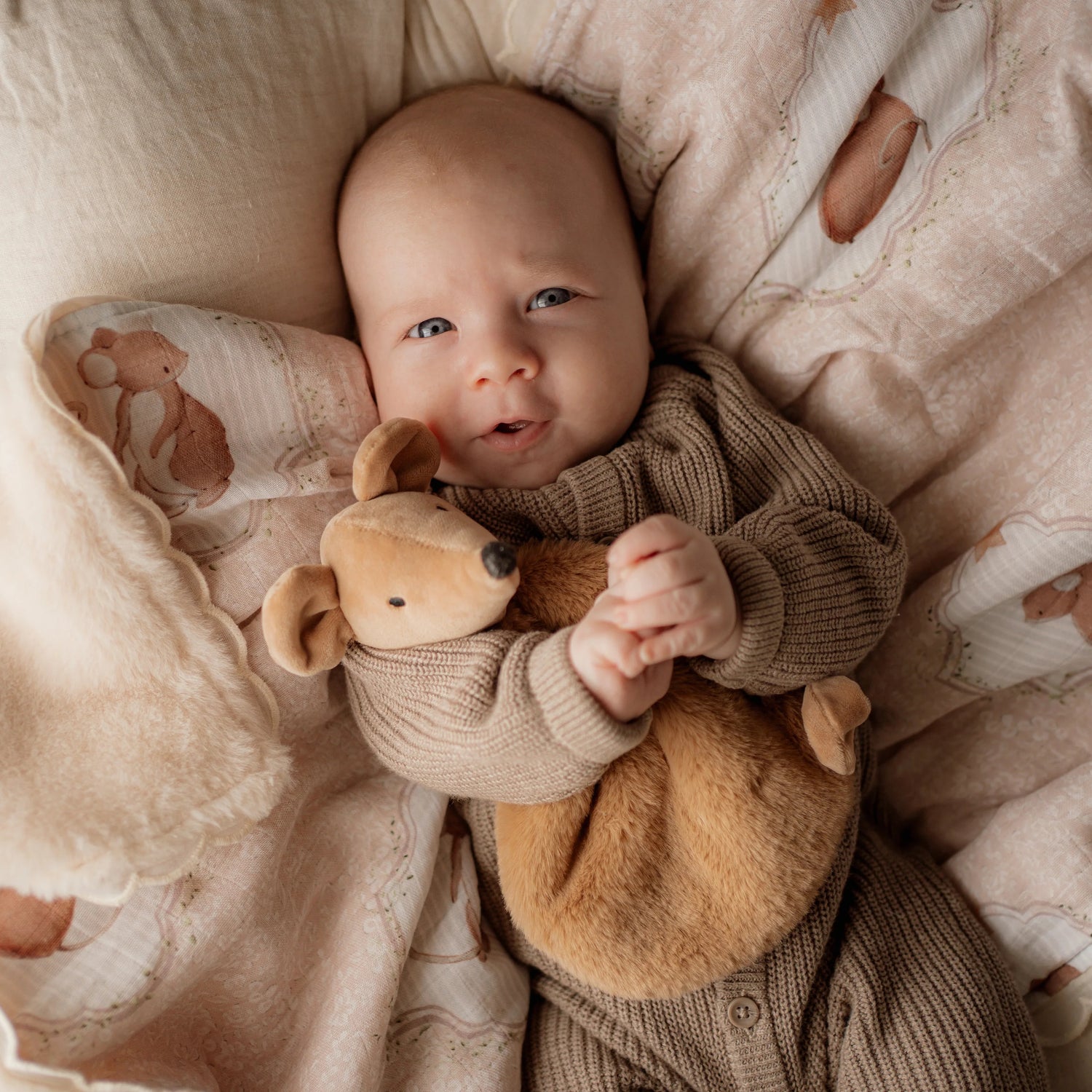 Baby holding a teddy mouse in a cozy, patterned crib