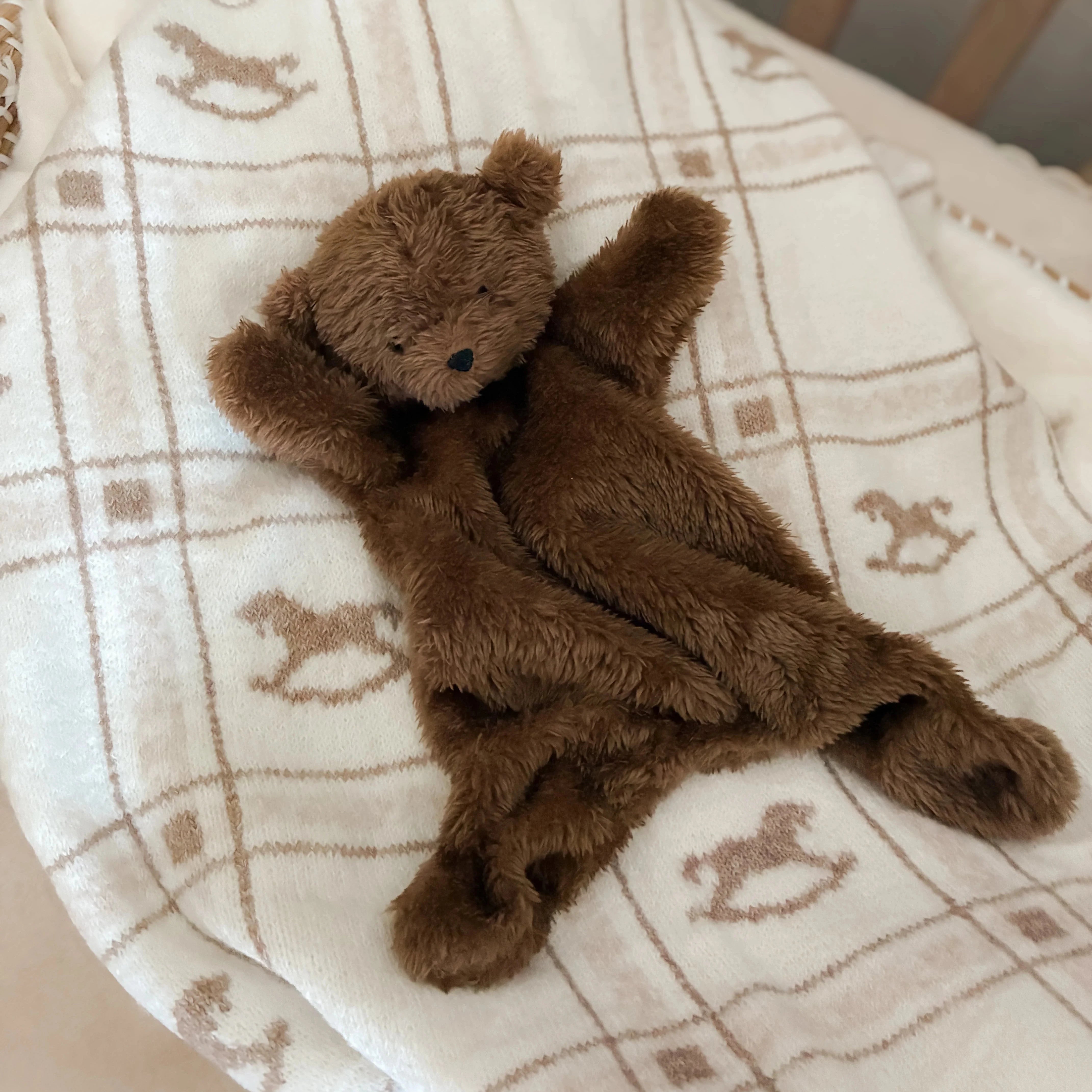 Brown teddy bear on a checkered blanket with rocking horse pattern