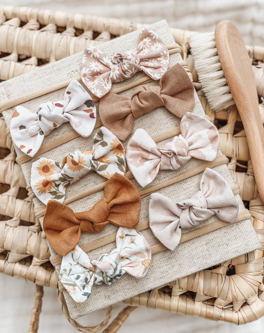 A collection of baby hairbows with various patterns and solid colors displayed on a woven mat.