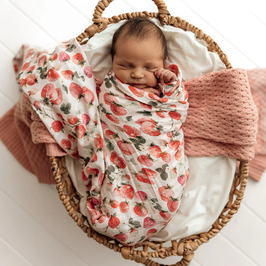 Newborn baby swaddled in a strawberry patterned blanket in a wicker basket.