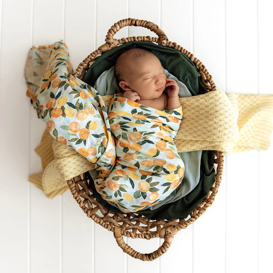 Newborn unisex baby swaddle gift a pale mint background with oranges scattered over it.
