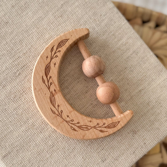Wooden crescent moon-shaped teething ring with engraved design on a textured fabric background
