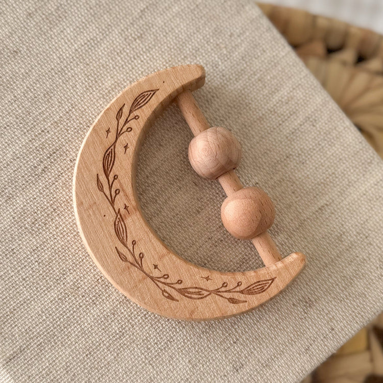 Wooden crescent moon-shaped teething ring with engraved design on a textured fabric background