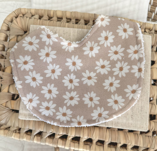 Neutral taupe baby bib featuring an all-over white daisy floral print with golden-yellow centres, contoured for comfort and handmade from soft cotton.