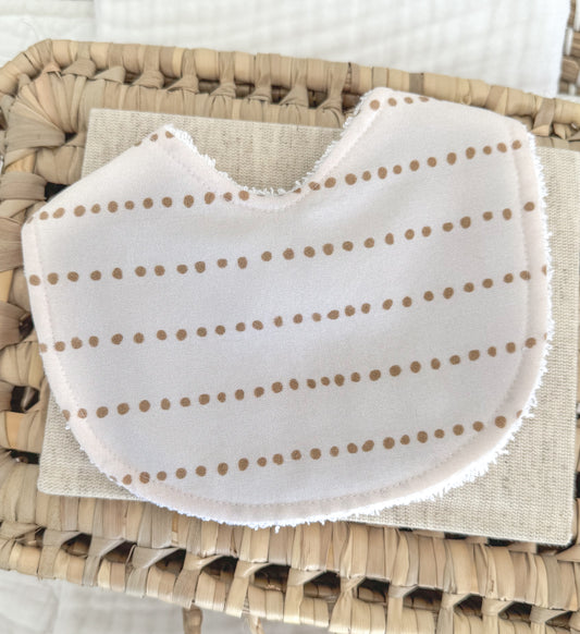 Handmade baby bib with a minimal dotted trail pattern in warm toffee brown on white cotton, contoured for newborn comfort and perfect as a unisex baby gift.