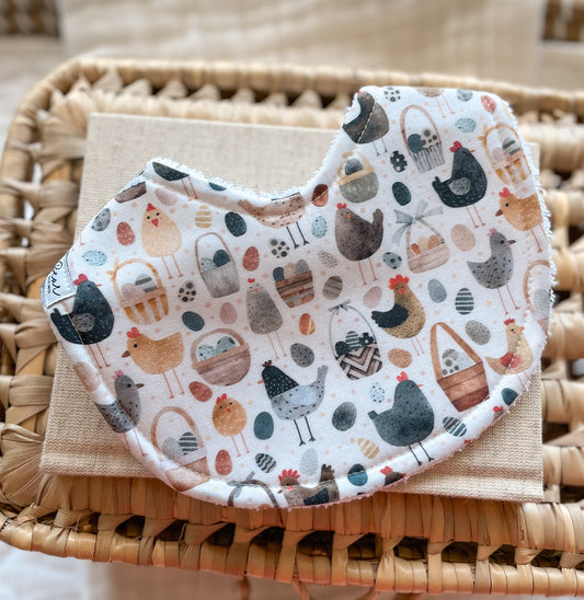 Handmade baby bib with illustrated chickens, farm eggs, and baskets in soft earthy tones, backed with absorbent terry towelling; perfect for teething or newborn messes.