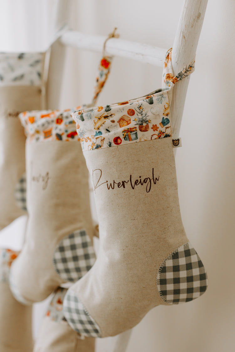 Personalised Christmas stocking handmade in beige fabric with toy and present print cuff and green gingham detail, customised with name.