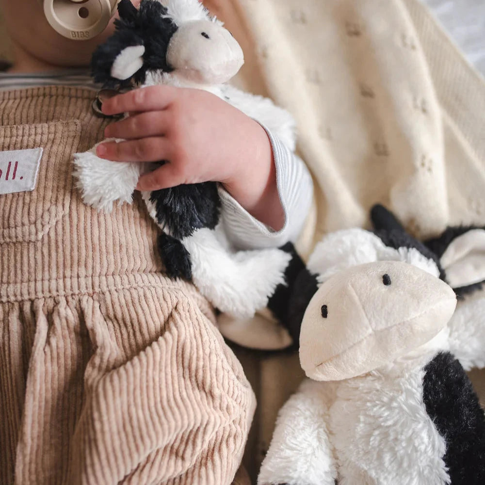 Baby holding a black and white farm cow toy. A bigger version of this toy lays beside him.