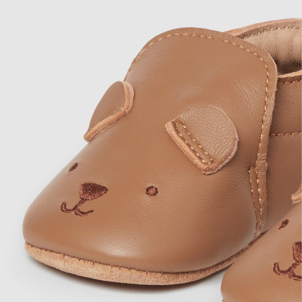 Brown leather baby shoes with a teddy bear face design on a light gray background