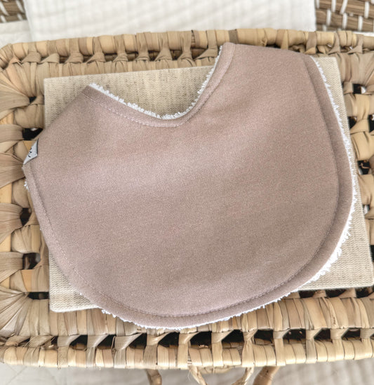 Handmade baby bib in solid dusky taupe cotton, featuring a contoured shape for newborn comfort and a gender-neutral design ideal for gifting.