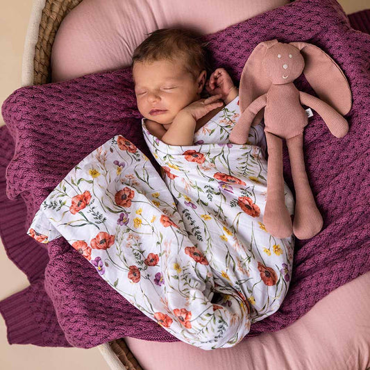 Newborn baby wrapped in a floral blanket with a plush toy in a basket