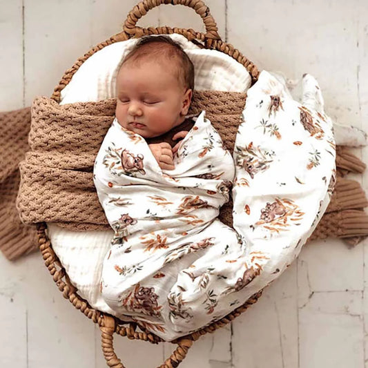 Newborn baby wrapped in a koala blanket in a wicker basket on a light wooden floor.