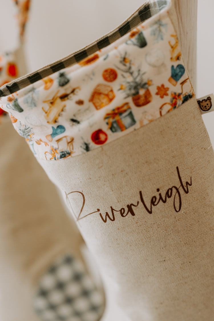 Personalised Christmas stocking handmade in beige fabric with green gingham detail and festive gift and Santa print cuff, customised with name Riverleigh.