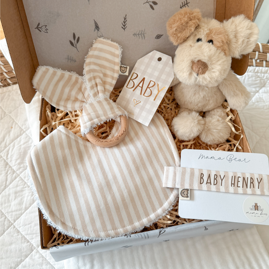 Gender Neutral baby gift box featuring a plush puppy dog toy, striped bib, teething ring, personalised baby name dummy clip, and a ‘Baby’ gift tag, beautifully packaged in a keepsake box with natural filler. 