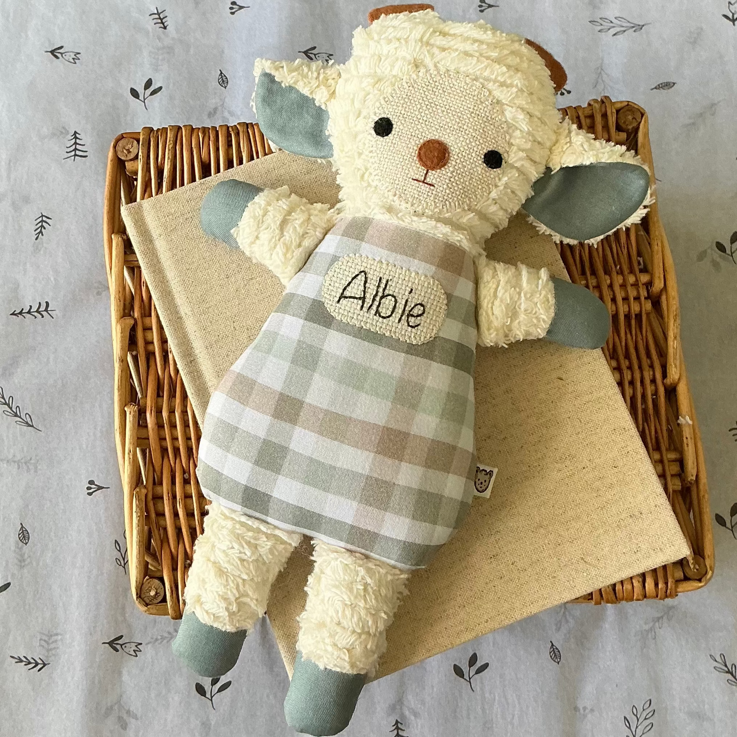 A handmade soft lamb keepsake. Lamb has white arms, legs and face. With blue paws and a blue, sage and brown gingham print  body. Hand stitched baby name in middle of lambs body. This would make a very unique newborn gift.