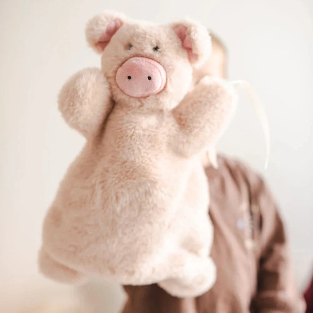 A person holding a blush pink piggy baby toy puppet.