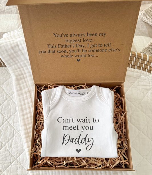 Pregnancy announcement box to gift husband / partner. On lid of the kraft box it says "you've always been my biggest love. This Father's Day, I get to tell you that soon, you'll be someone else's whole world too." inside box is a white onesie that says "Can't wait to meet you Daddy"/