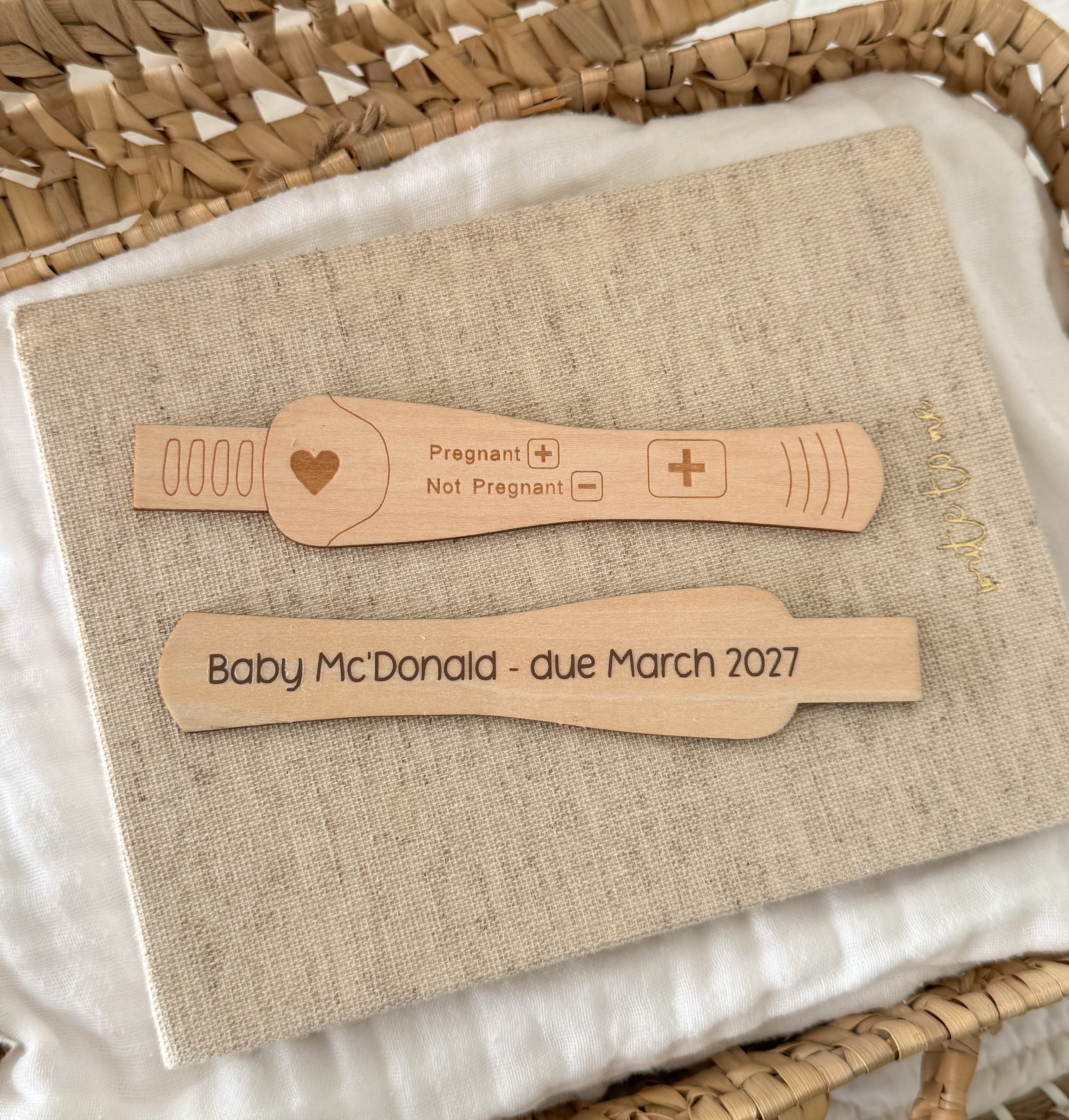 Two personalised wooden pregnancy test sticks are displayed. The top test is engraved with a heart and 'Pregnant / Not Pregnant' options with  '+' meaning pregnant. And the bottom test is customised with 'Baby McDonald - due March 2027'.