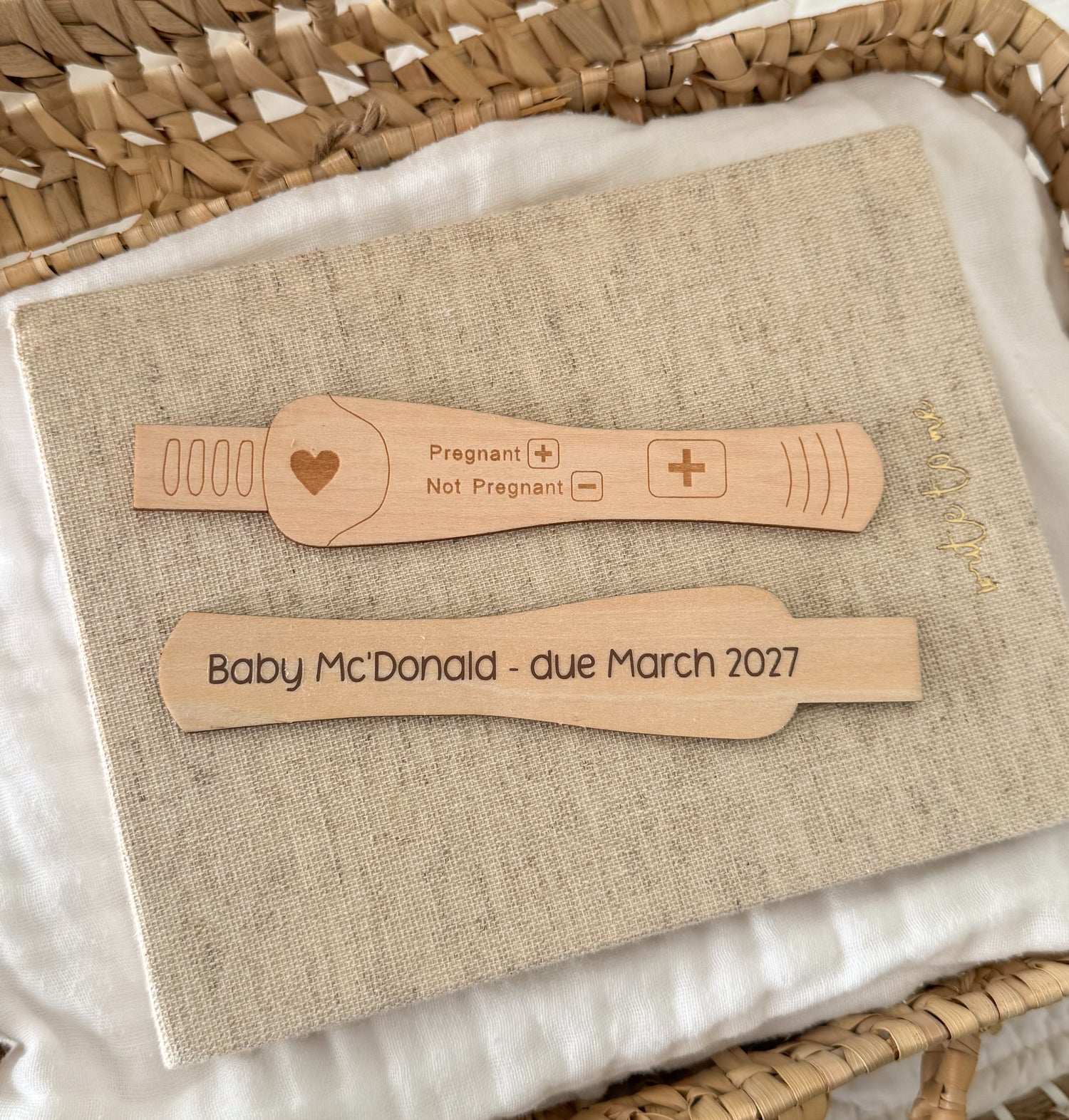 Two personalised wooden pregnancy test sticks are displayed. The top test is engraved with a heart and 'Pregnant / Not Pregnant' options with  '+' meaning pregnant. And the bottom test is customised with 'Baby McDonald - due March 2027'.