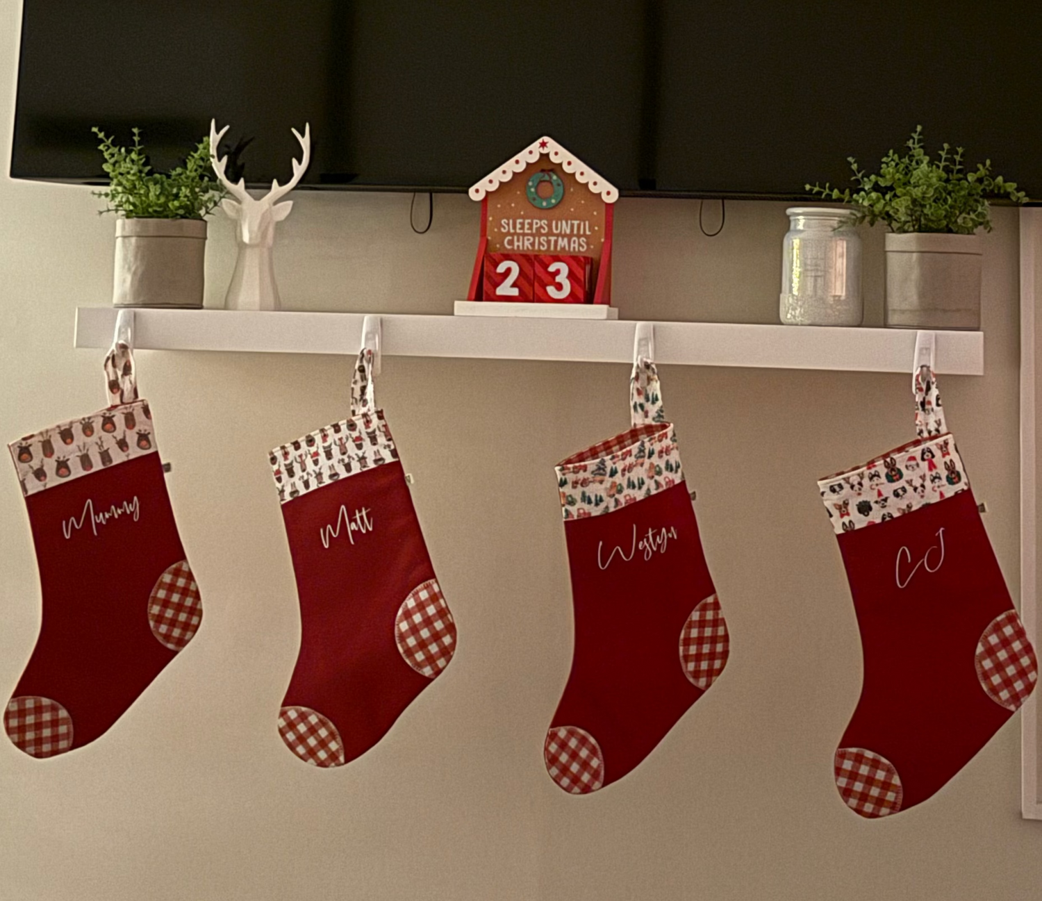 Four red Christmas stockings with white trim with pictures of reindeers on the fabric hanging from a white shelf 