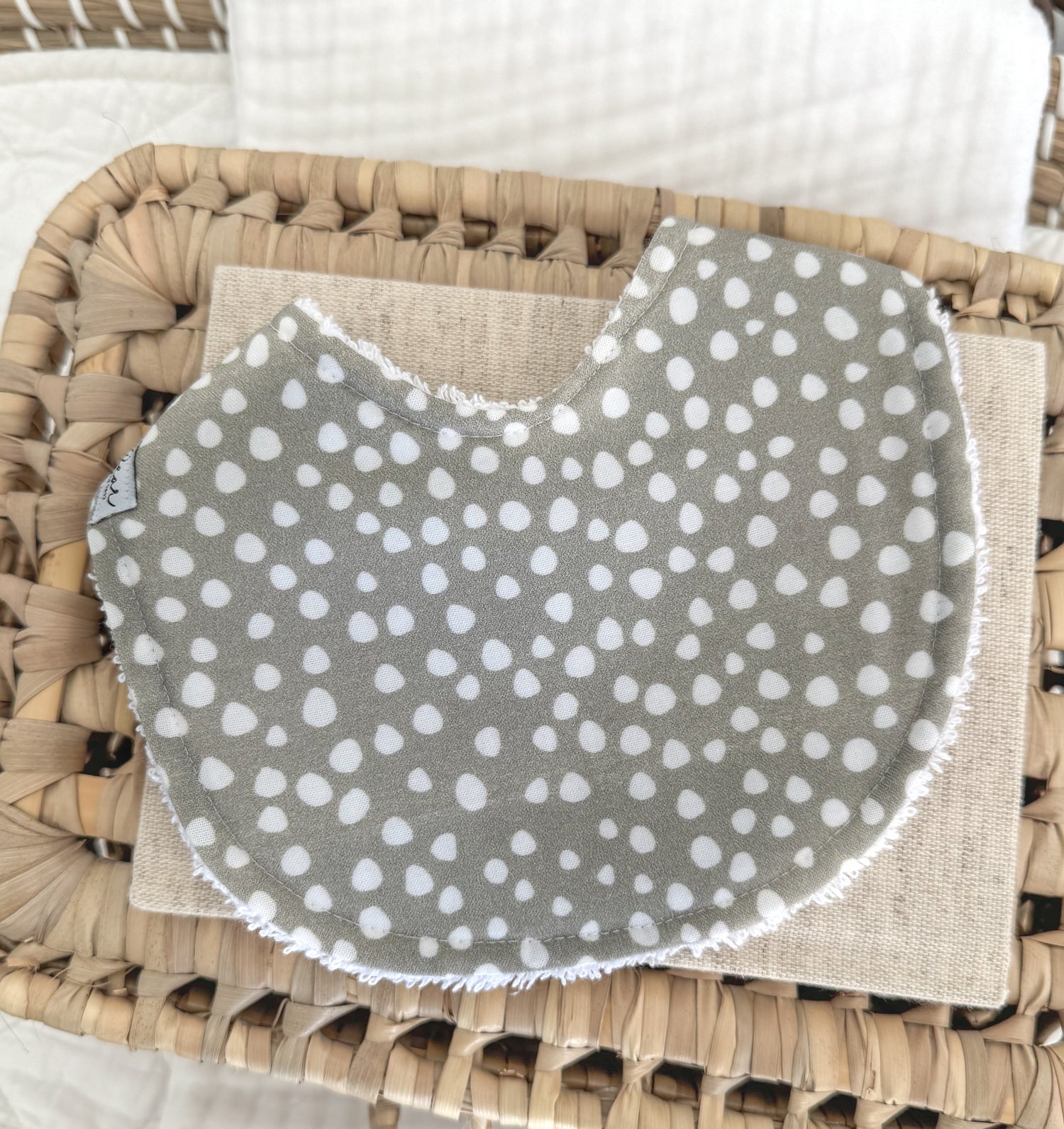 Handmade baby bib featuring a white sprinkle dot pattern on muted sage green cotton, contoured for newborn comfort and a beautiful gender-neutral gift option.