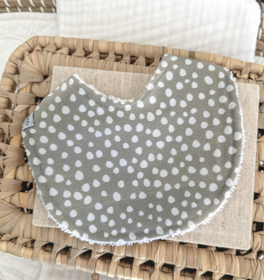 Handmade baby bib featuring a white sprinkle dot pattern on muted sage green cotton, contoured for newborn comfort and a beautiful gender-neutral gift option.
