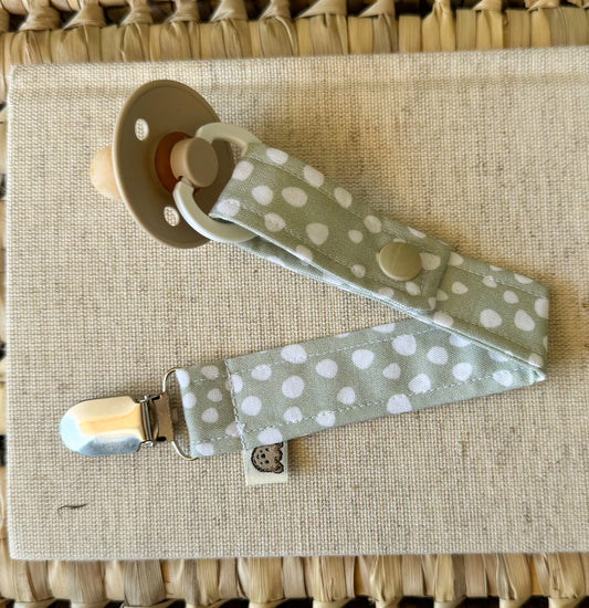 A baby dummy clip in sage green material with white polka dots.