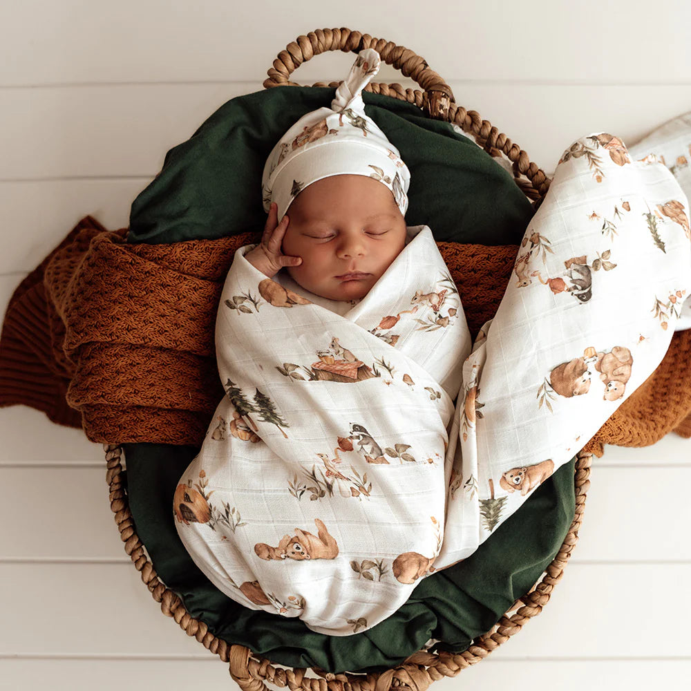 Newborn baby swaddled in a basket with a bear pattern, wearing a matching hat.