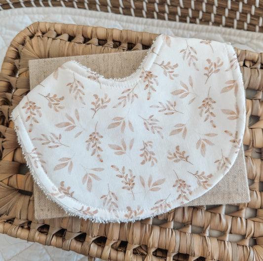 Bib with a white background scattered with light beige illustrations of leaves.