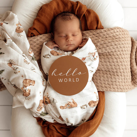 Newborn baby swaddled in a white muslin blanket with cute bear illustrations on it. 