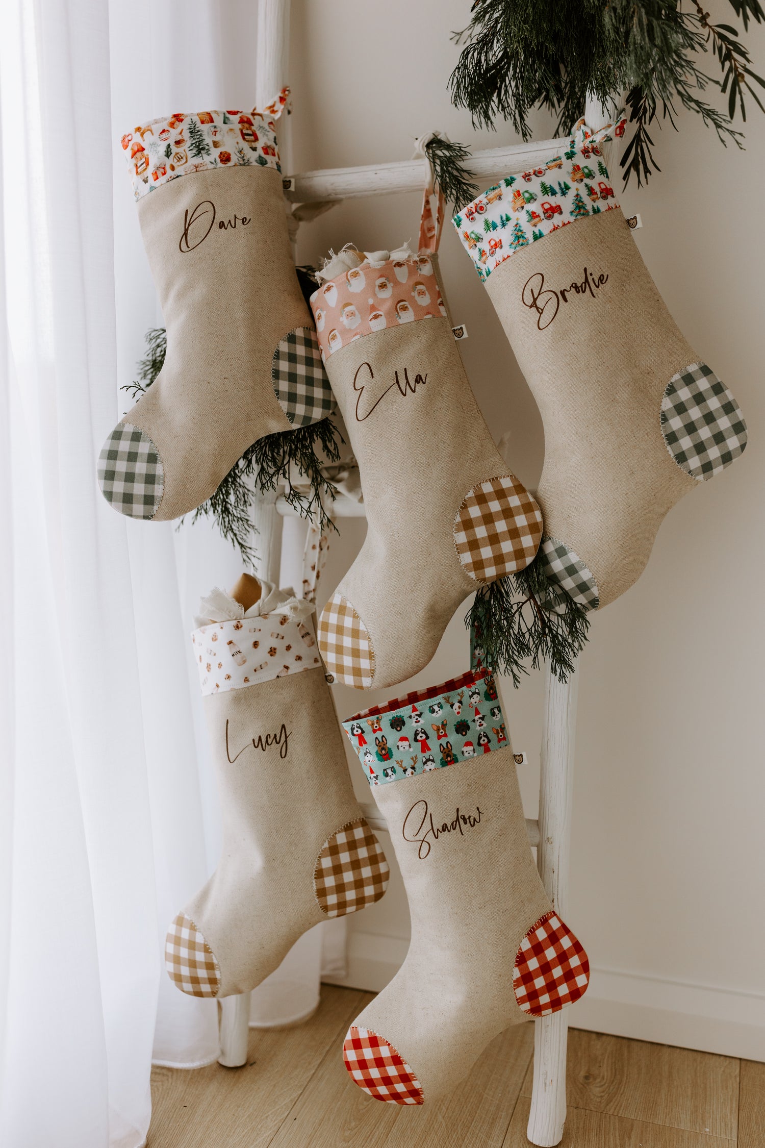 Handmade personalised Christmas stocking in natural linen with the name “Dave” in brown script font, featuring a festive Santa Claus print cuff with reindeer, Christmas trees and gifts, and finished with sage green gingham heel and toe patches. Rustic farmhouse style holiday stocking, custom made in Australia, ideal for family or children’s Christmas décor.