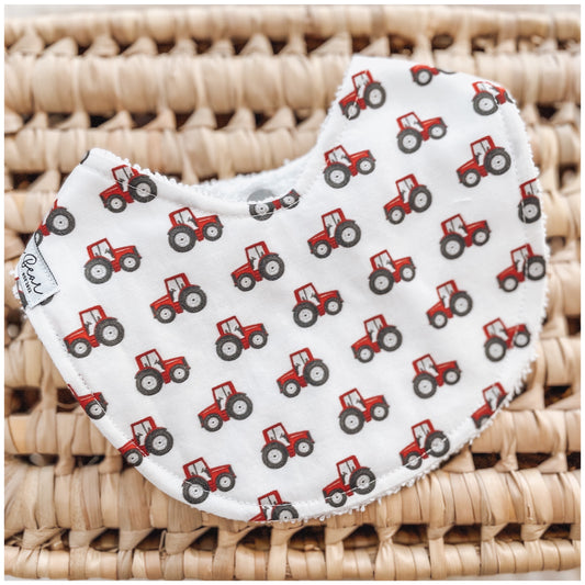 Baby bib with all-over red tractors print on a white background.