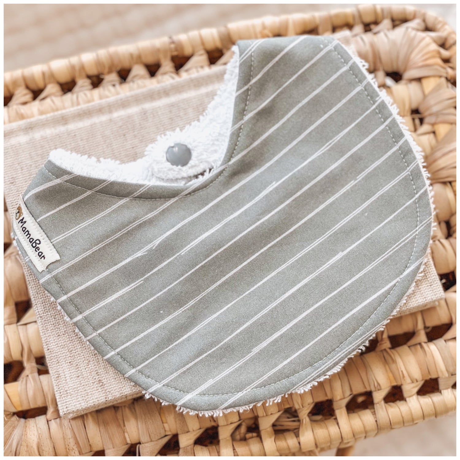 Neutral sage green baby bib with fine white stripes, made from soft cotton and absorbent terry towelling backing.