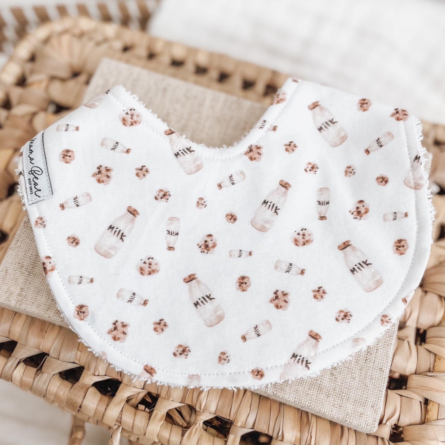 White baby bib printed with mini milk bottles and chocolate chip cookies. Features terry towelling backing for absorbency—great for dribble, teething, or feeding.