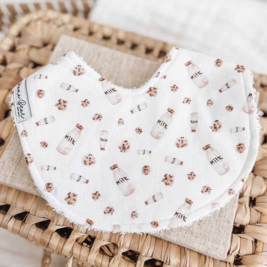 White baby bib printed with mini milk bottles and chocolate chip cookies. Features terry towelling backing for absorbency—great for dribble, teething, or feeding.