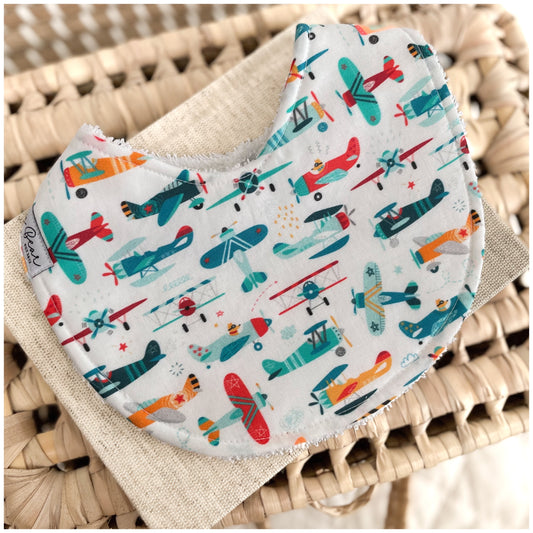 Baby bib with a white background featuring a colourful print of vintage-style airplanes and cartoon tigers in teal, red, orange, and navy, backed with white terry towelling.