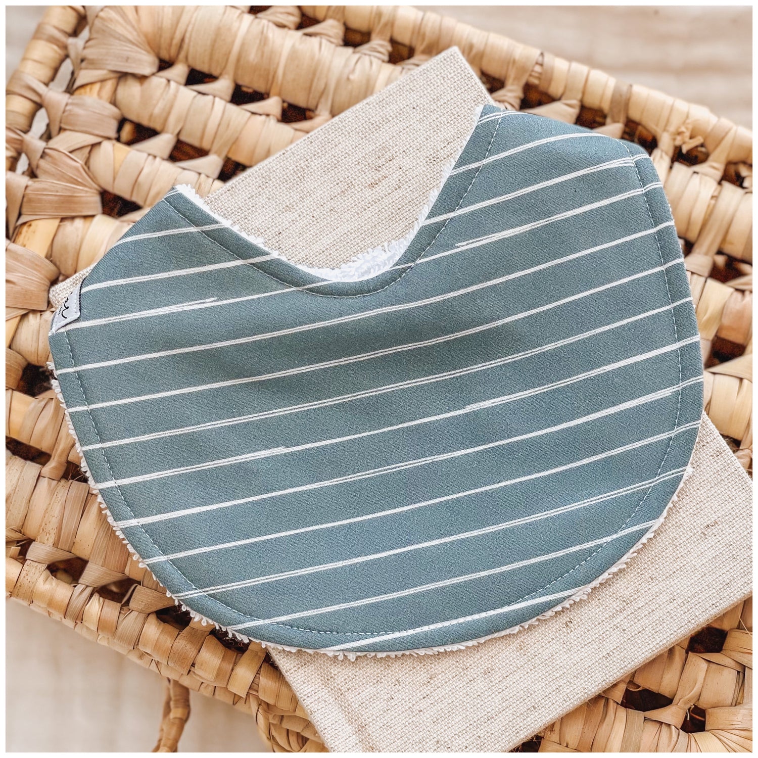 Baby bib featuring a cobalt blue fabric with white pinstripes, displayed on a woven basket with a neutral linen cloth.