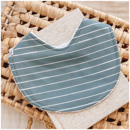 Baby bib featuring a cobalt blue fabric with white pinstripes, displayed on a woven basket with a neutral linen cloth.