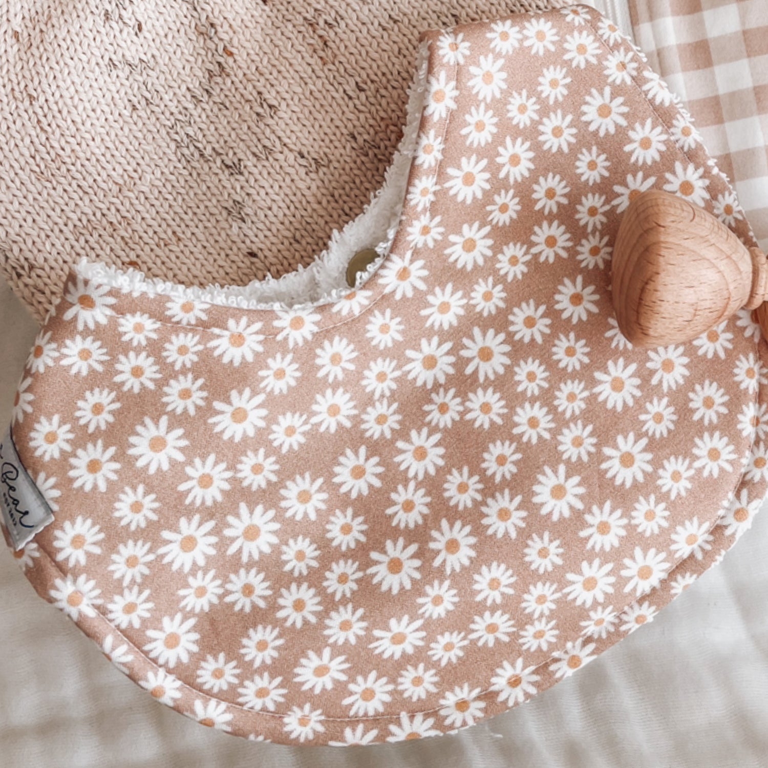 Baby bib with white daisy flower pattern on a muted clay-pink background, backed with soft terry towelling for absorbency. Ideal for teething, drool, and feeding.