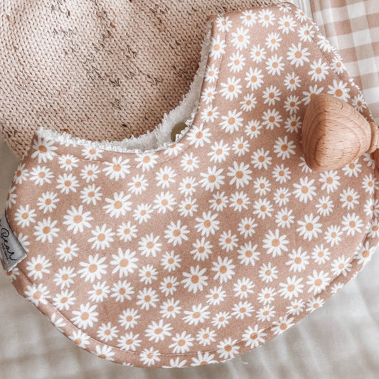 Baby bib with white daisy flower pattern on a muted clay-pink background, backed with soft terry towelling for absorbency. Ideal for teething, drool, and feeding.