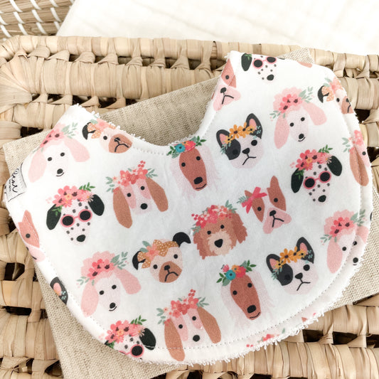 White baby bib with a fun dog print—featuring cartoon-style puppies wearing flower crowns, bows, and sunglasses. Absorbent terry towelling backing, ideal for teething and feeding.