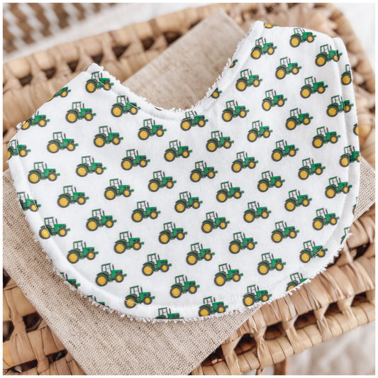 White baby bib featuring a repeated pattern of small green and yellow tractors, backed with absorbent terry towelling fabric.