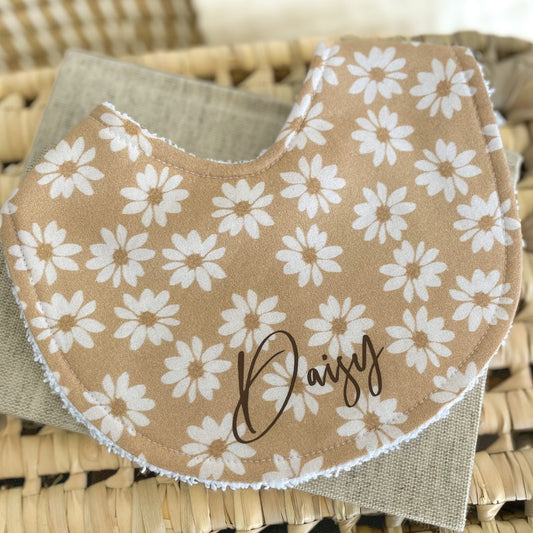 Personalised baby bib with white daisy flowers on a caramel brown background, shown with the name “Daisy” in script. Soft terry towelling backing, ideal for dribbles and feeding.