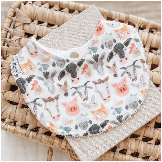Farm-themed baby bib with cute illustrated animals including cows, pigs, donkeys, ducks, bunnies, and cats on a white background.