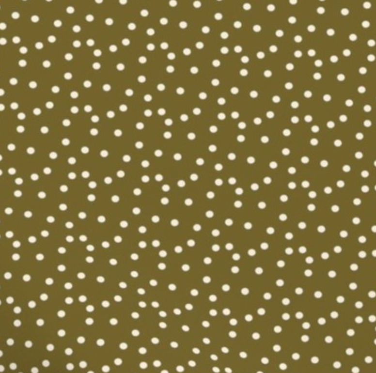 Sage green baby bib with a white polka dot print, styled on a woven basket with a neutral cloth underneath.