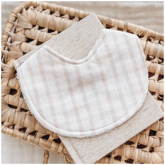 Neutral baby bib with soft beige and white vertical gingham stripes, made from cotton with an absorbent terry towelling backing.