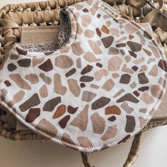 Modern baby bib with terrazzo-style print in warm earthy tones and soft white terry towelling backing.