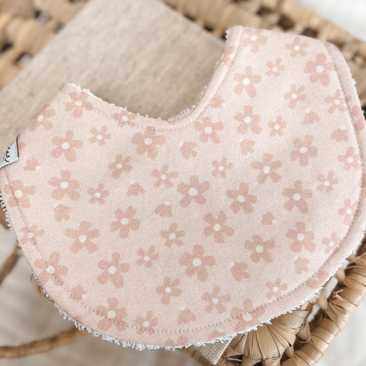 Blush pink baby bib with a soft daisy pattern on a pale peach background. Features absorbent terry towelling backing, perfect for newborns and teething.
